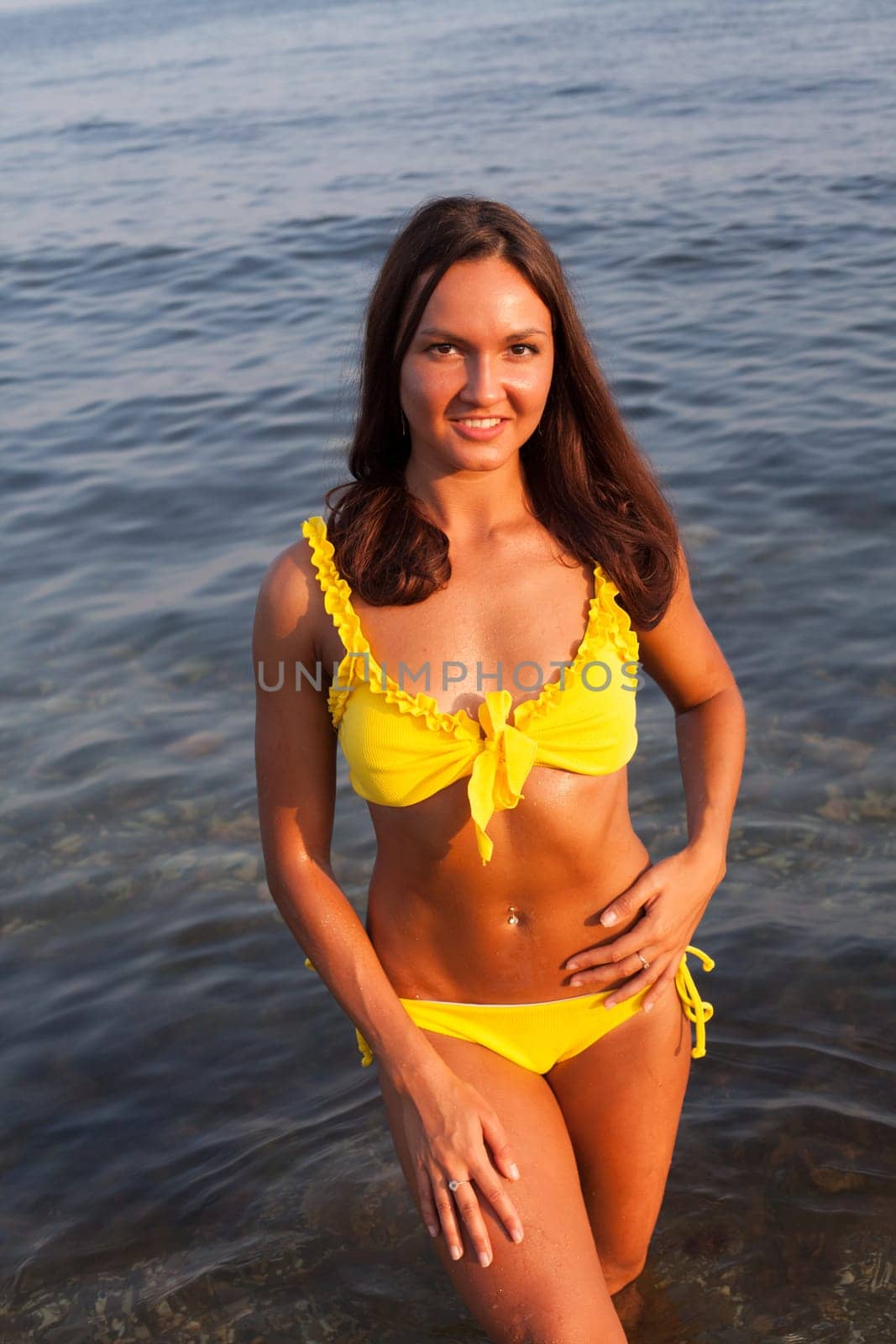 woman with long hair in a yellow swimsuit walks on the beach by the sea