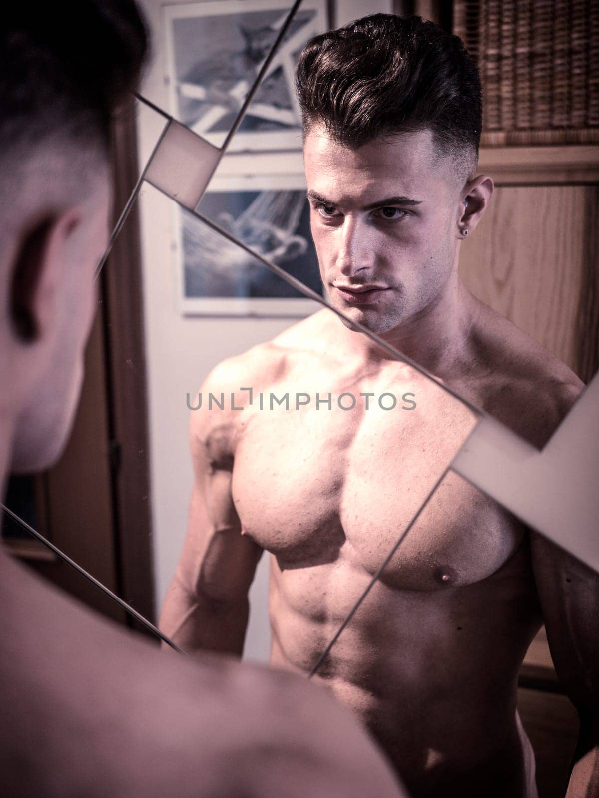 A shirtless muscular man looking at himself in the mirror