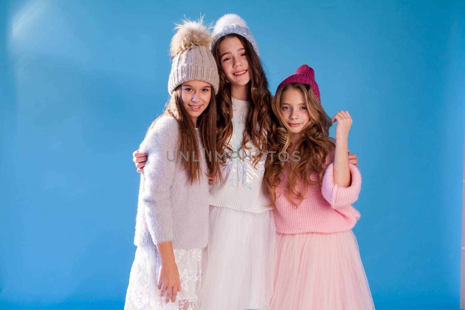 Three beautiful fashionable girl girlfriends in a winter snow cap blue background