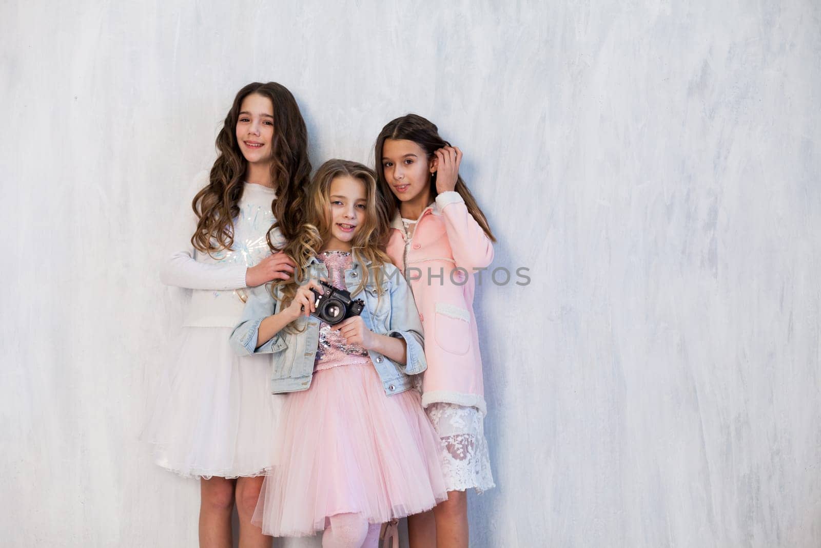 Portrait of three beautiful girlfriend girls with a camera in white pink clothes