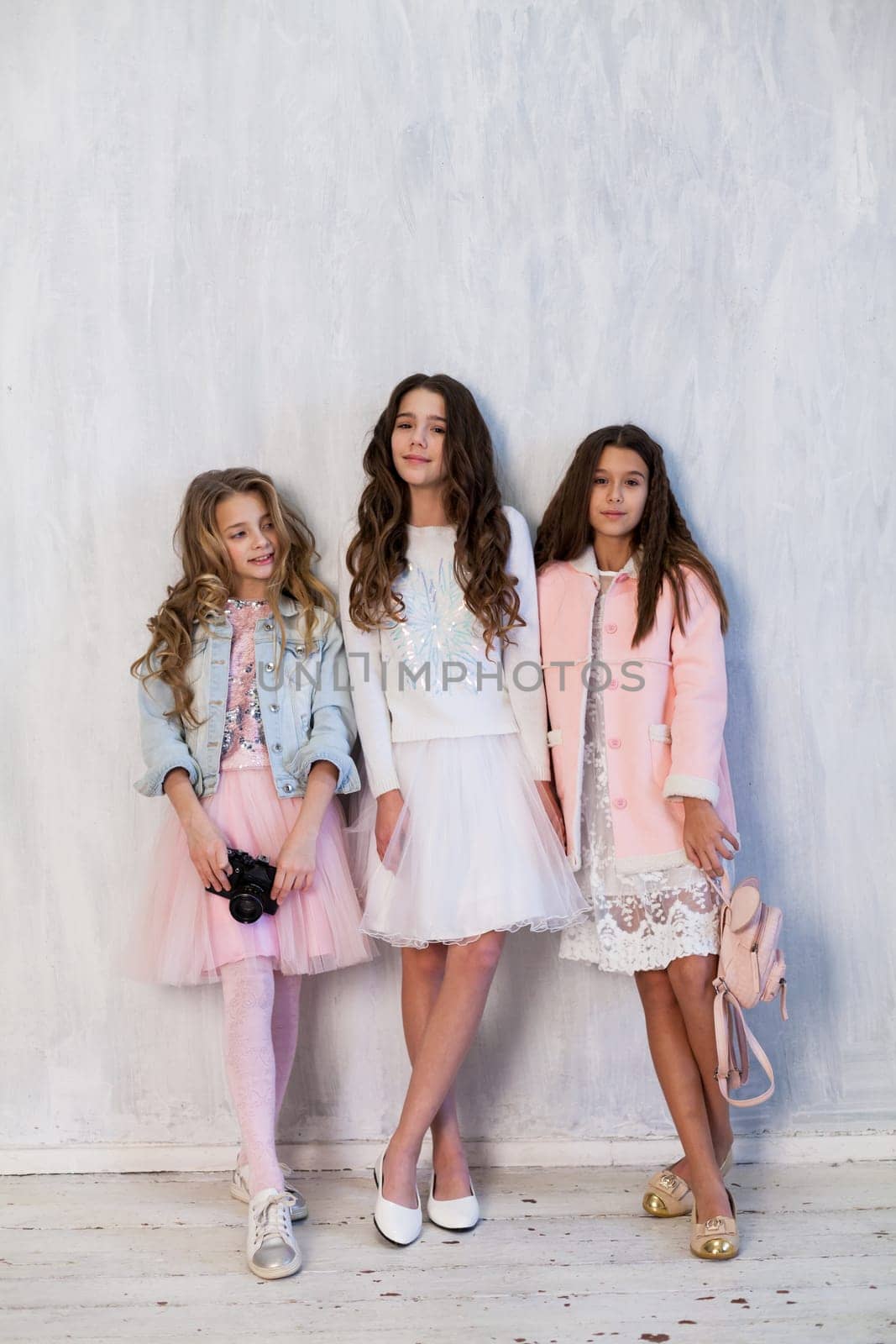 Portrait of three beautiful girlfriend girls with a camera in white pink clothes