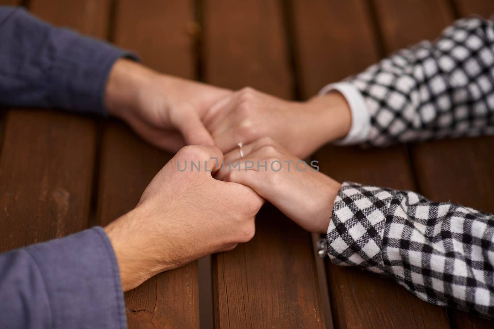 Close up on a man and a woman holding hands at a wooden table. Loving couple holding hands on table, man friend husband support woman wife expressing love feelings, trust care honesty in interracial relationship concept, close up view by Andrii_Ko