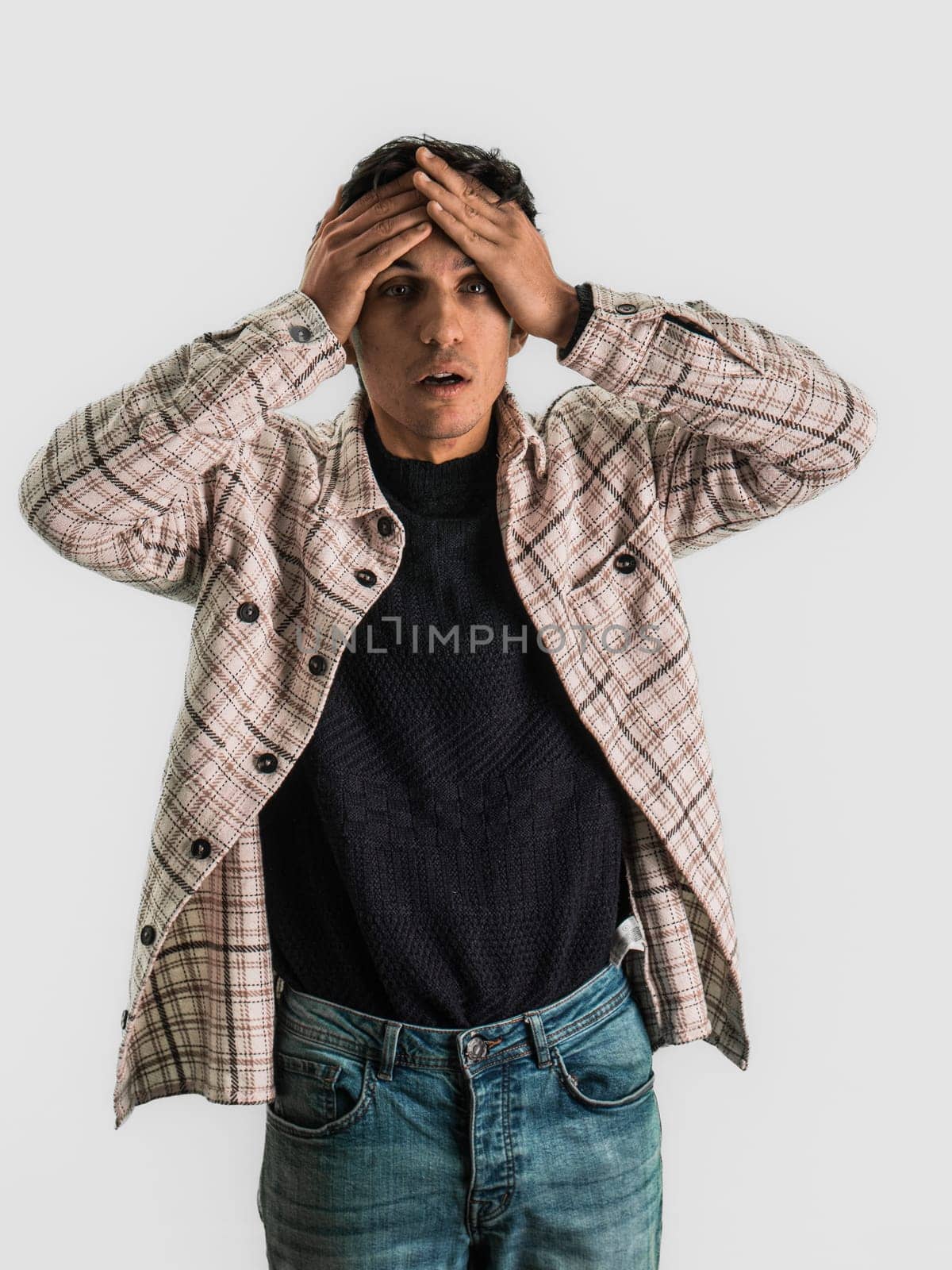 Depressed or sad handsome young man with head in his hands in a desperation concept, in studio shot. Desperate, upset young man with hands on his face and looking at camera