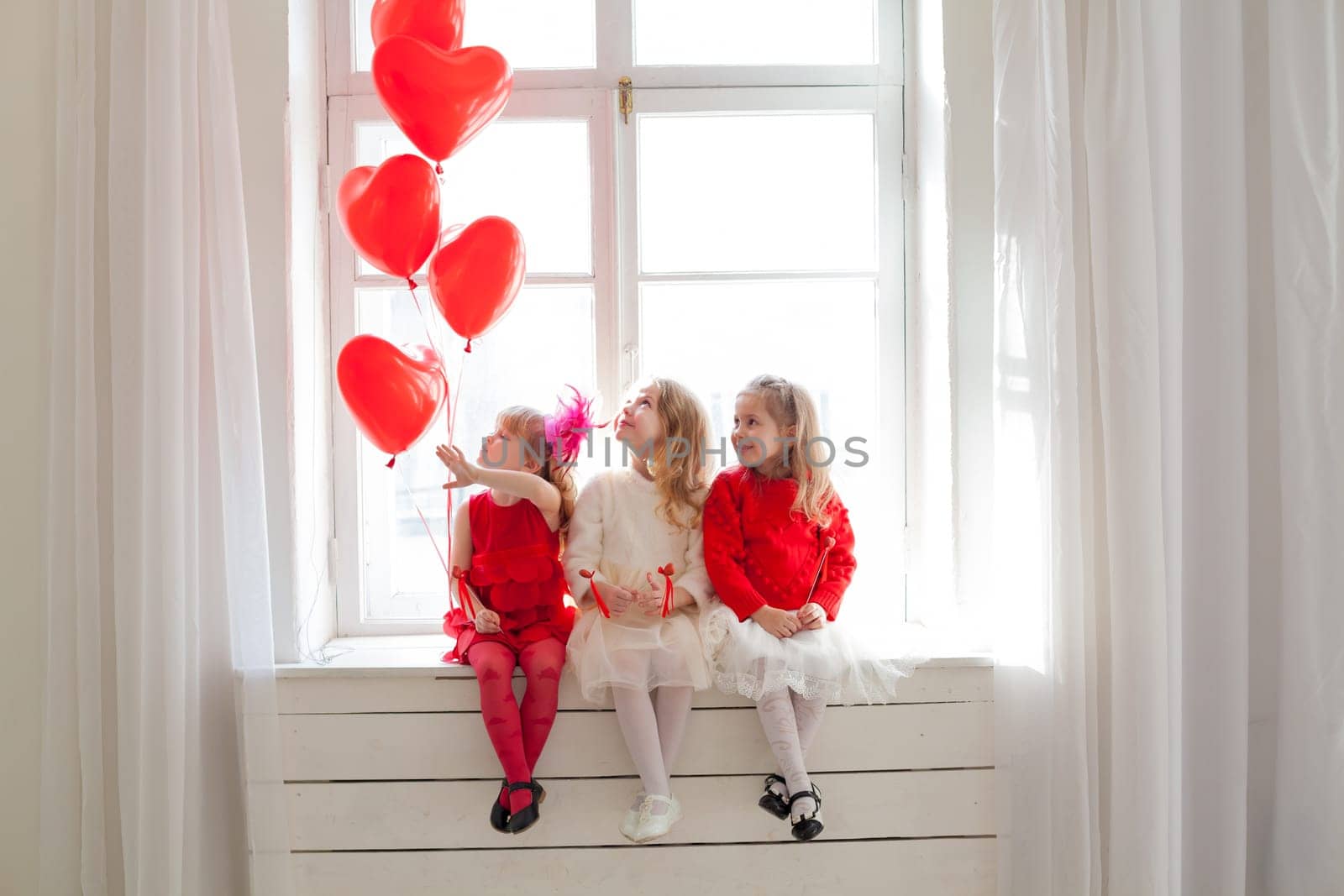 Three girls with red balloons in the shape of a heart on holiday by Simakov