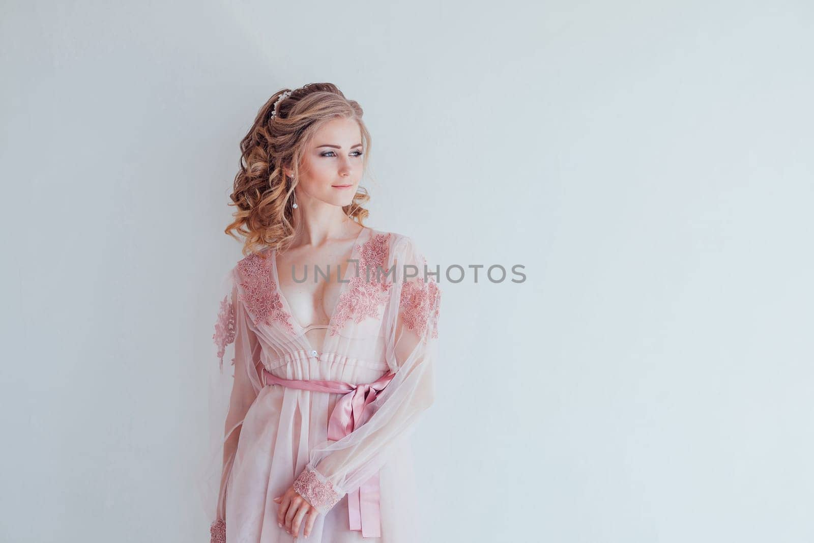 pretty girl in pink lingerie stands at white walls bride