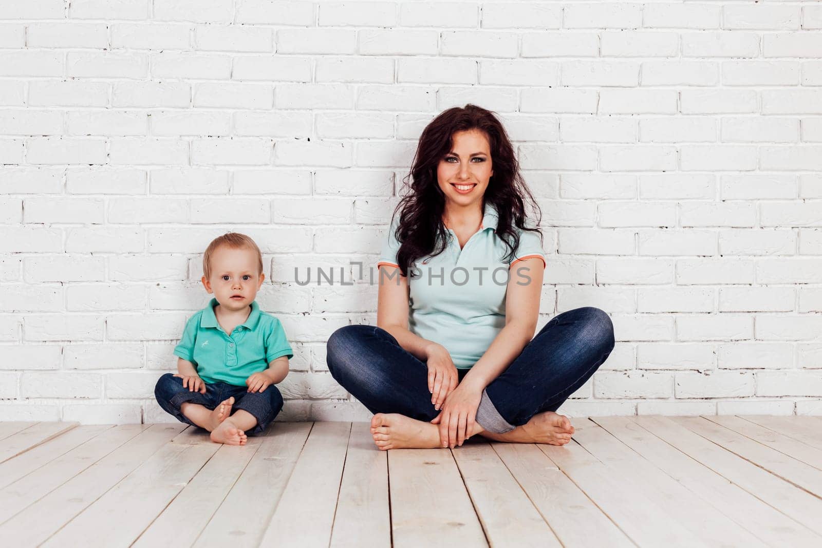 mom and young boy son sit on the floor white brick wall