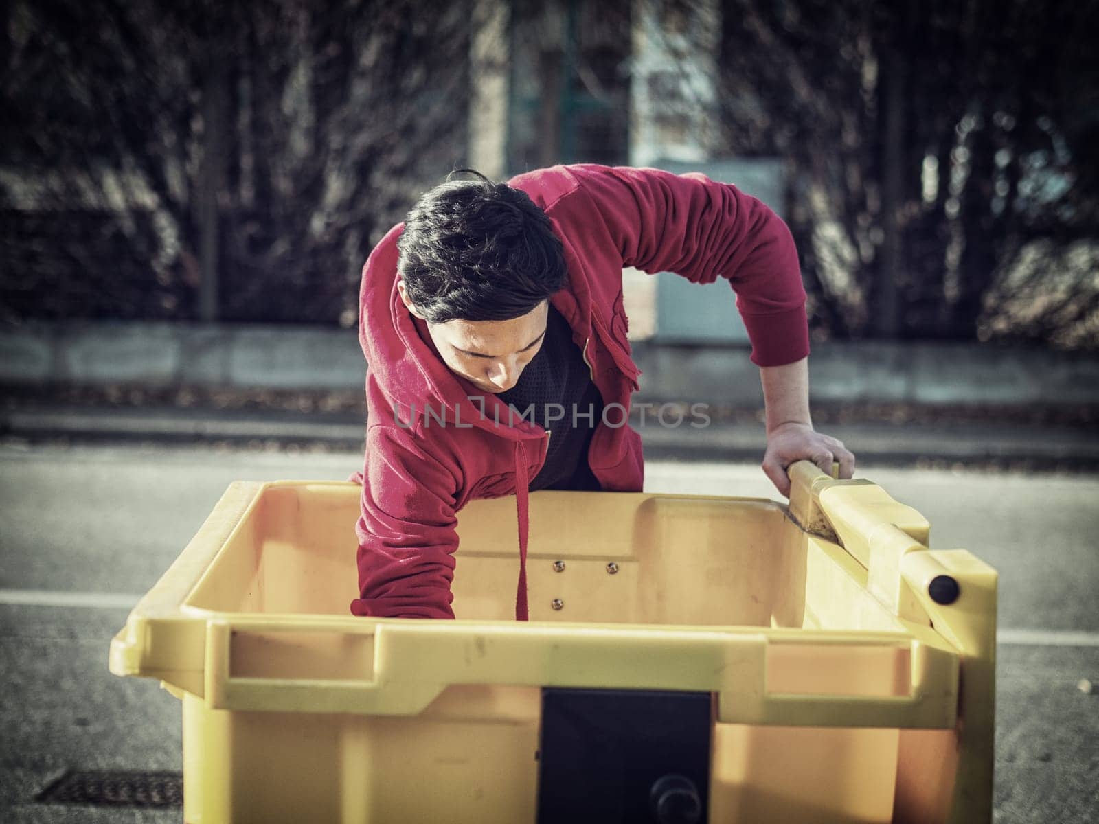 Young poor man searching inside garbage bin for stuff still usable or useful