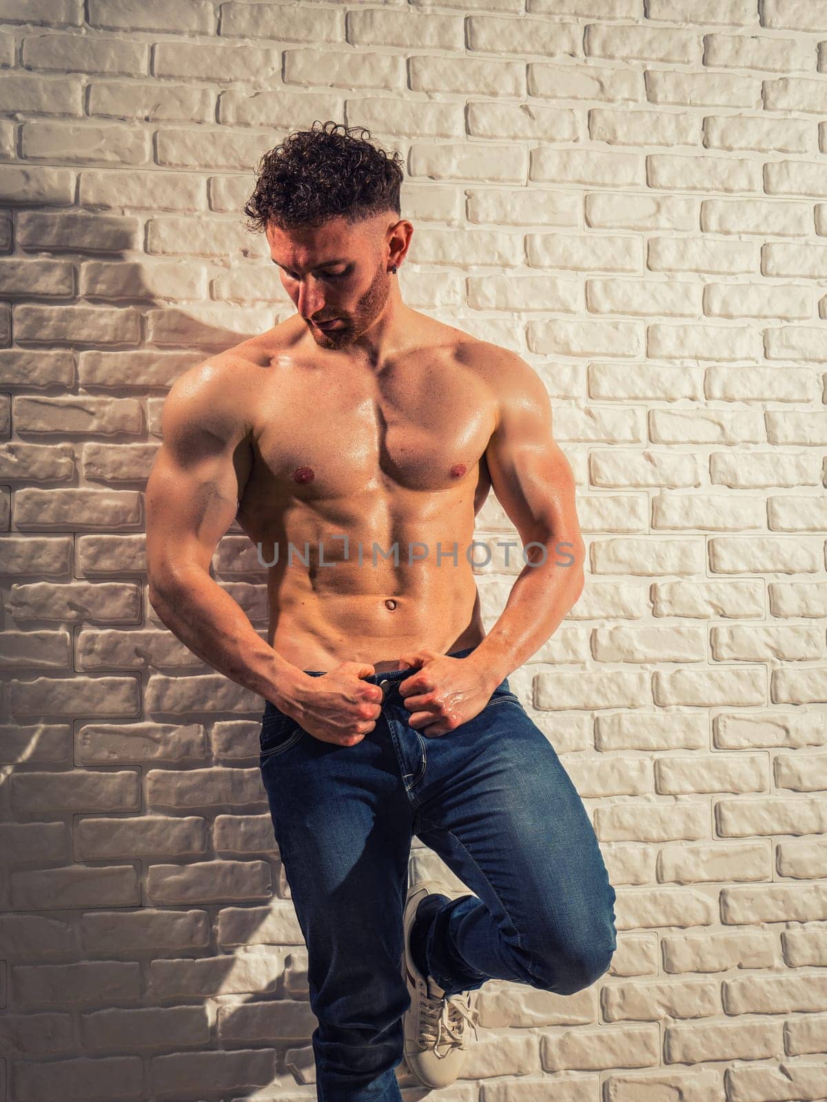 A shirtless man leaning against a brick wall