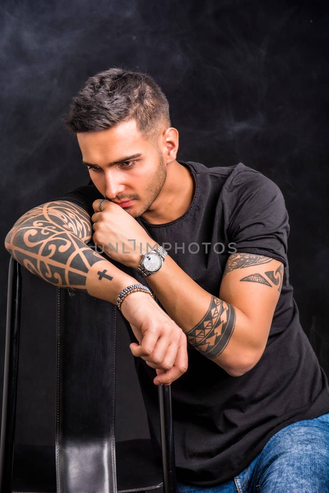 A man with tattoos sitting on a chair. Photo of a man with vibrant tattoos sitting on a stylish chair