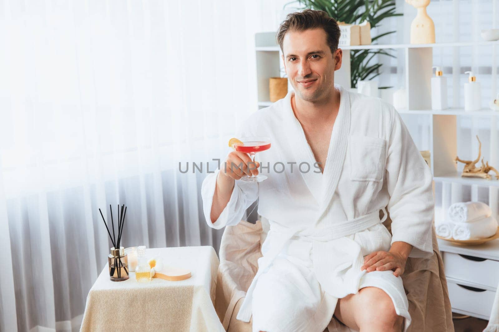 Beauty or body treatment spa salon vacation lifestyle concept with man wearing bathrobe relaxing with drinks in luxurious hotel spa or resort room. Vacation and leisure relaxation. Quiescent