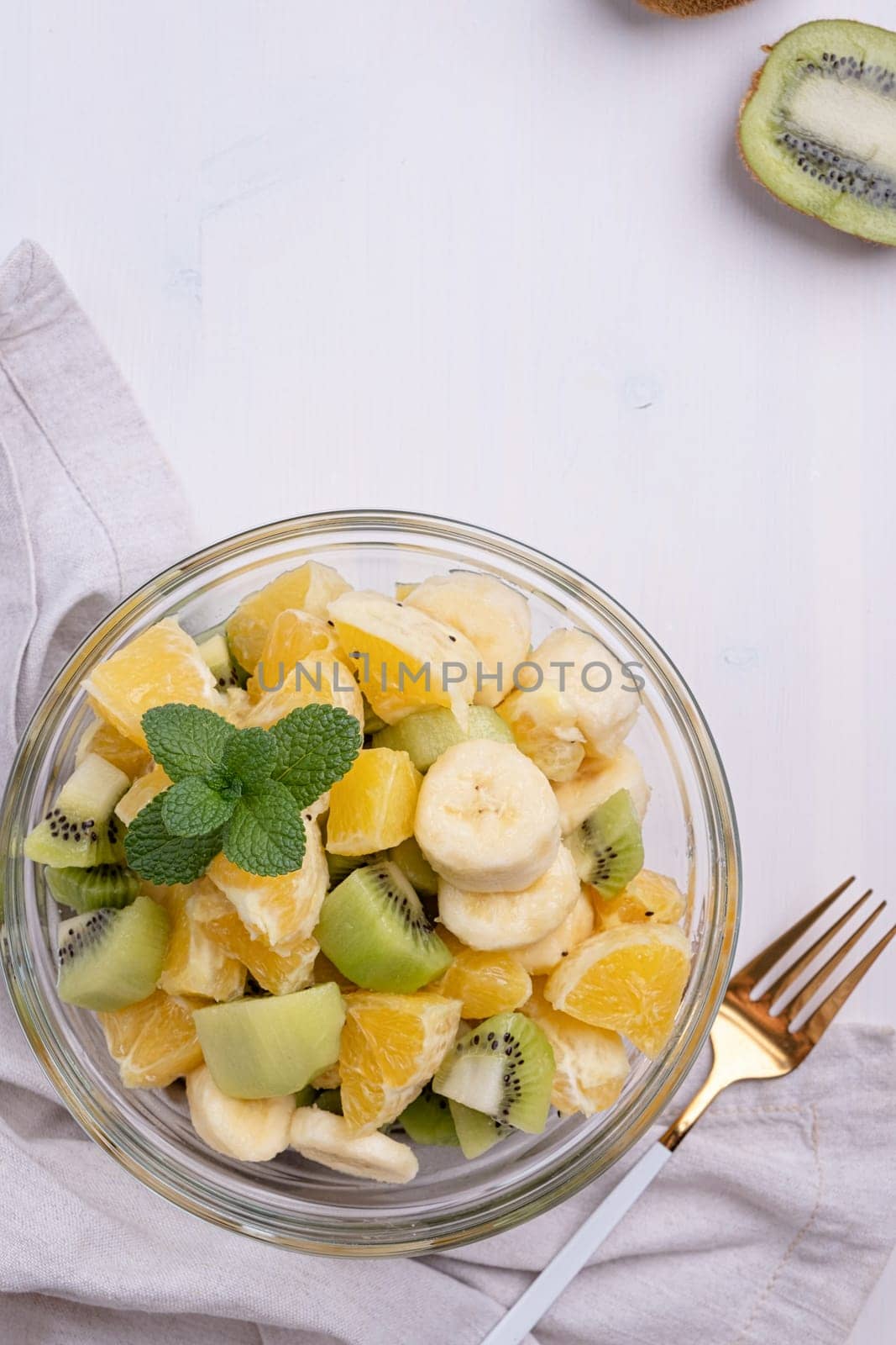 Bowl of healthy fresh fruit salad on white wooden background. Top view.