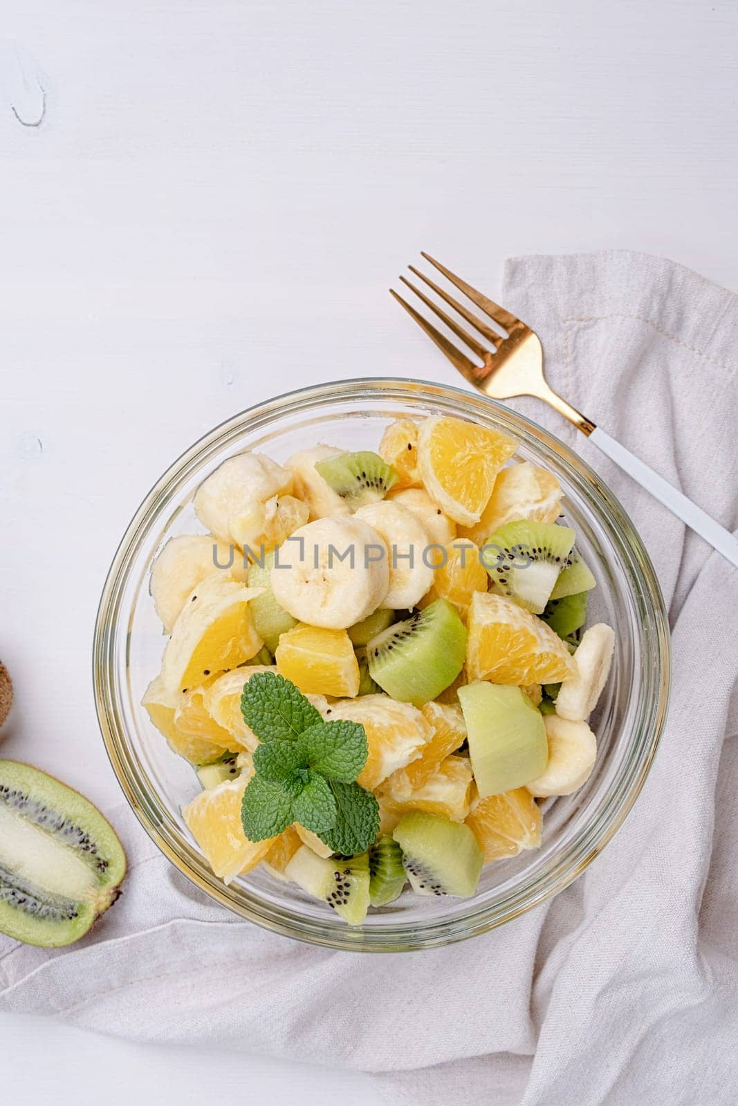 Bowl of healthy fresh fruit salad on white wooden background. Top view.