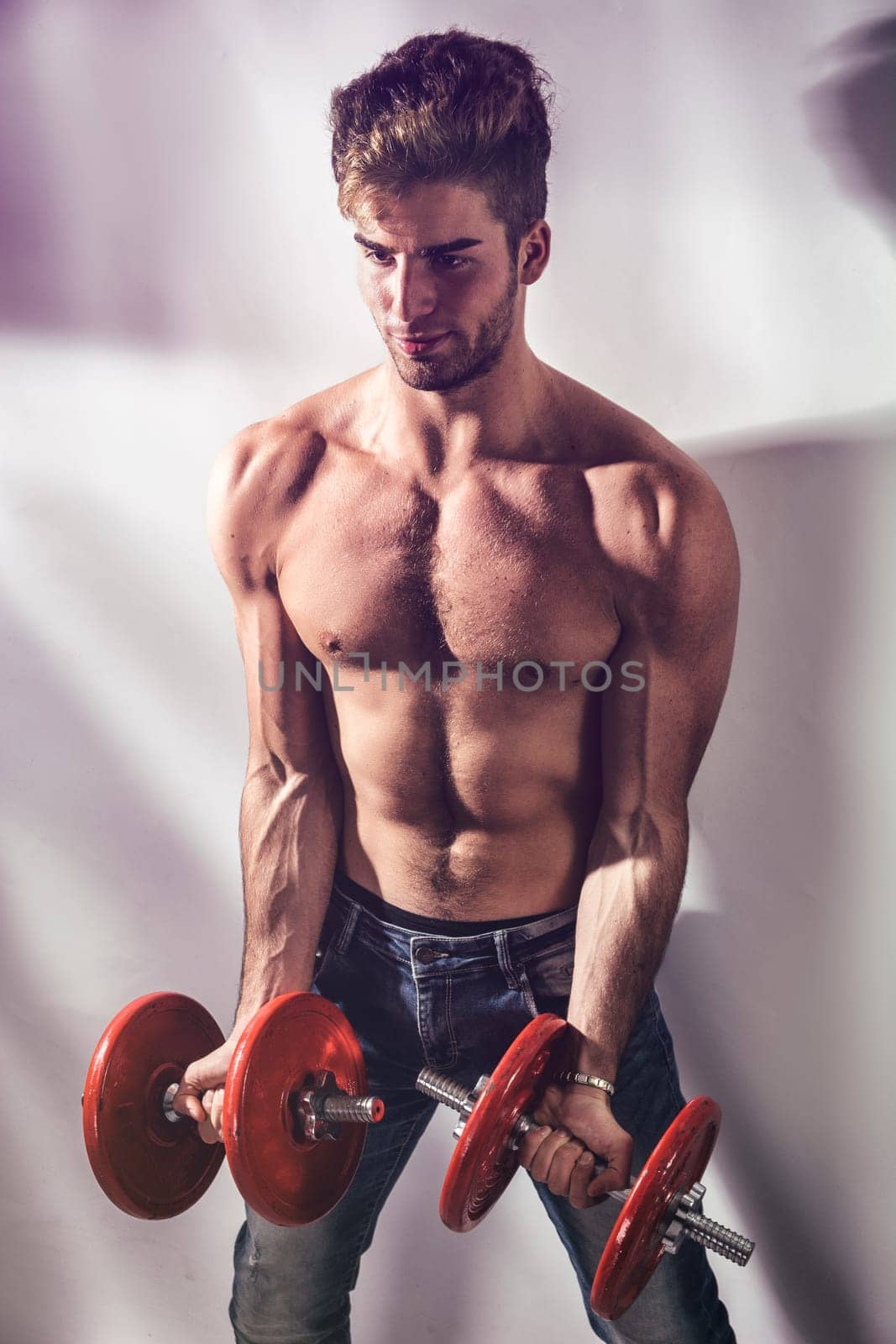 A shirtless man holding two red dumbs