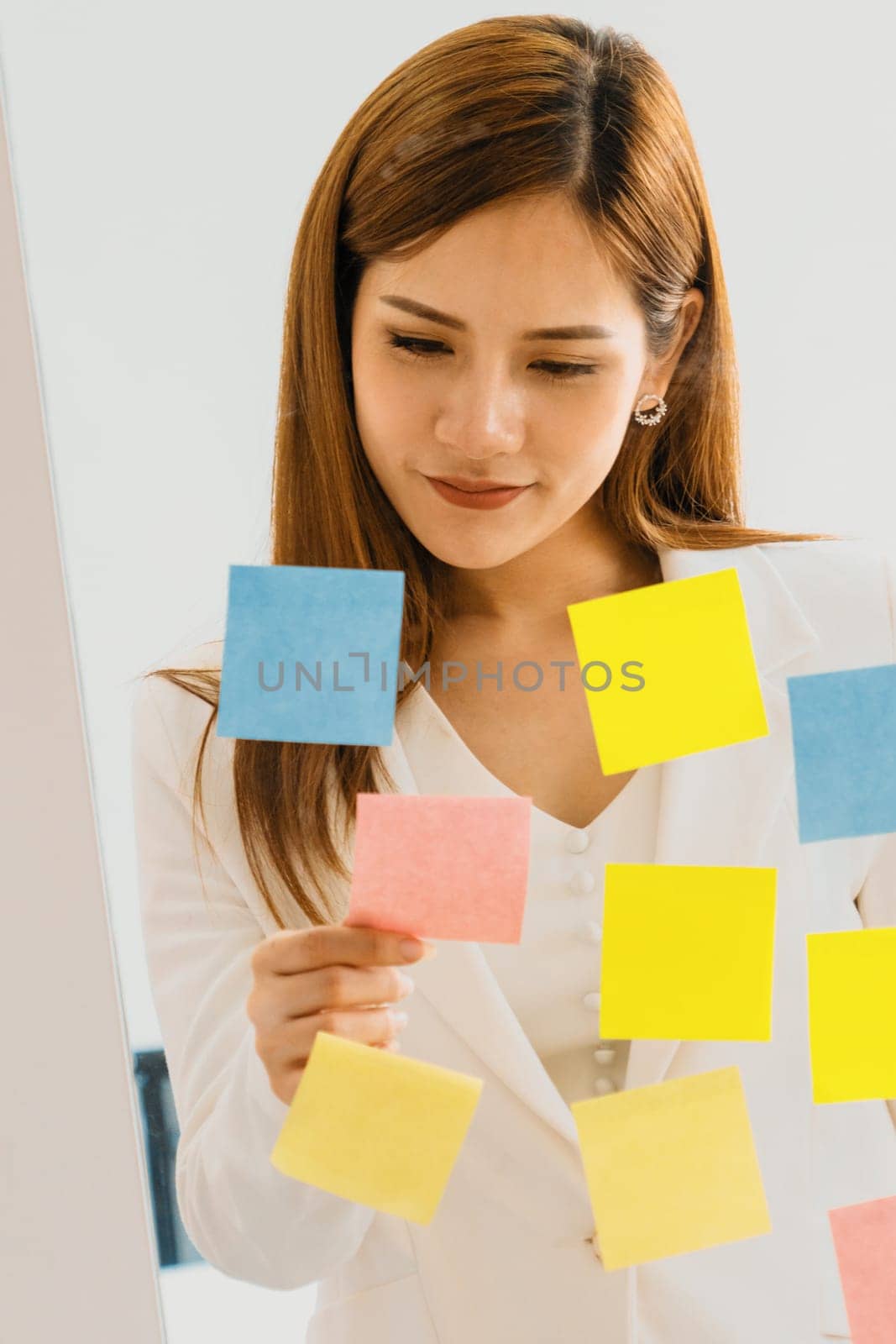 Happy businesswoman thinking creative ideas with sticky notes on glass wall at the office. Work planning and education concept uds