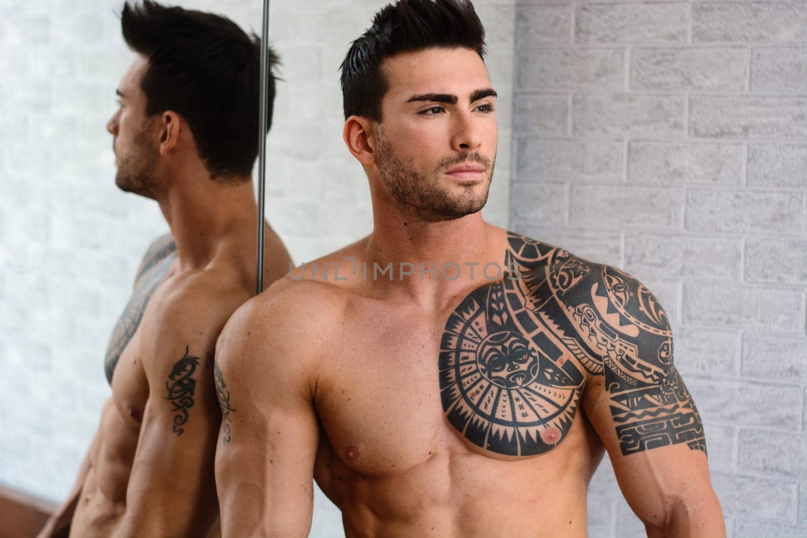 A handsome muscular man with tattoos standing in front of a mirror