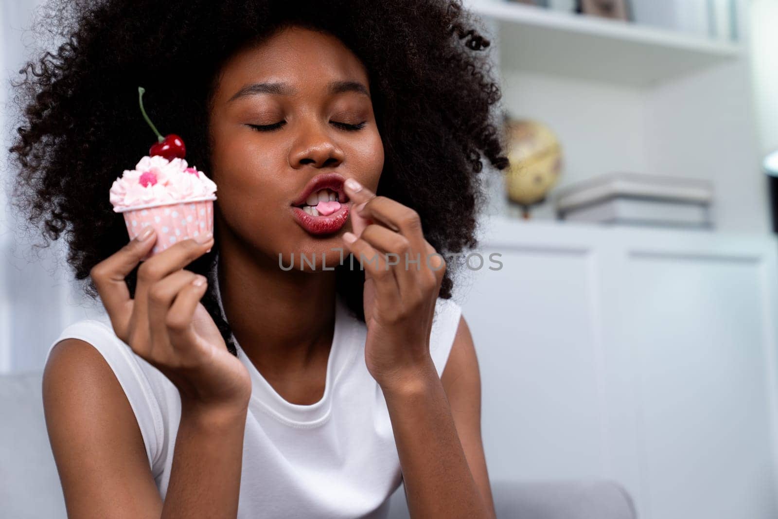 Portrait of beautiful young African blogger tasting piece of cherry cake in concept special cuisine. Presenting cute cupcake decorate fruit for content creating on social media. Tastemaker.