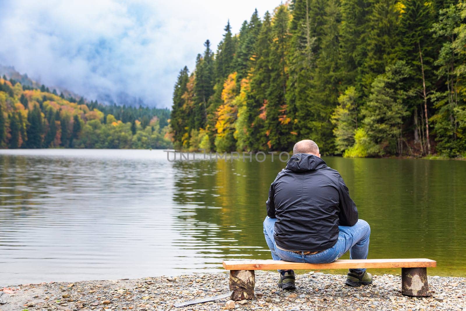 A man admires a picturesque view by a lake in the mountains surrounded by the beauty of nature.