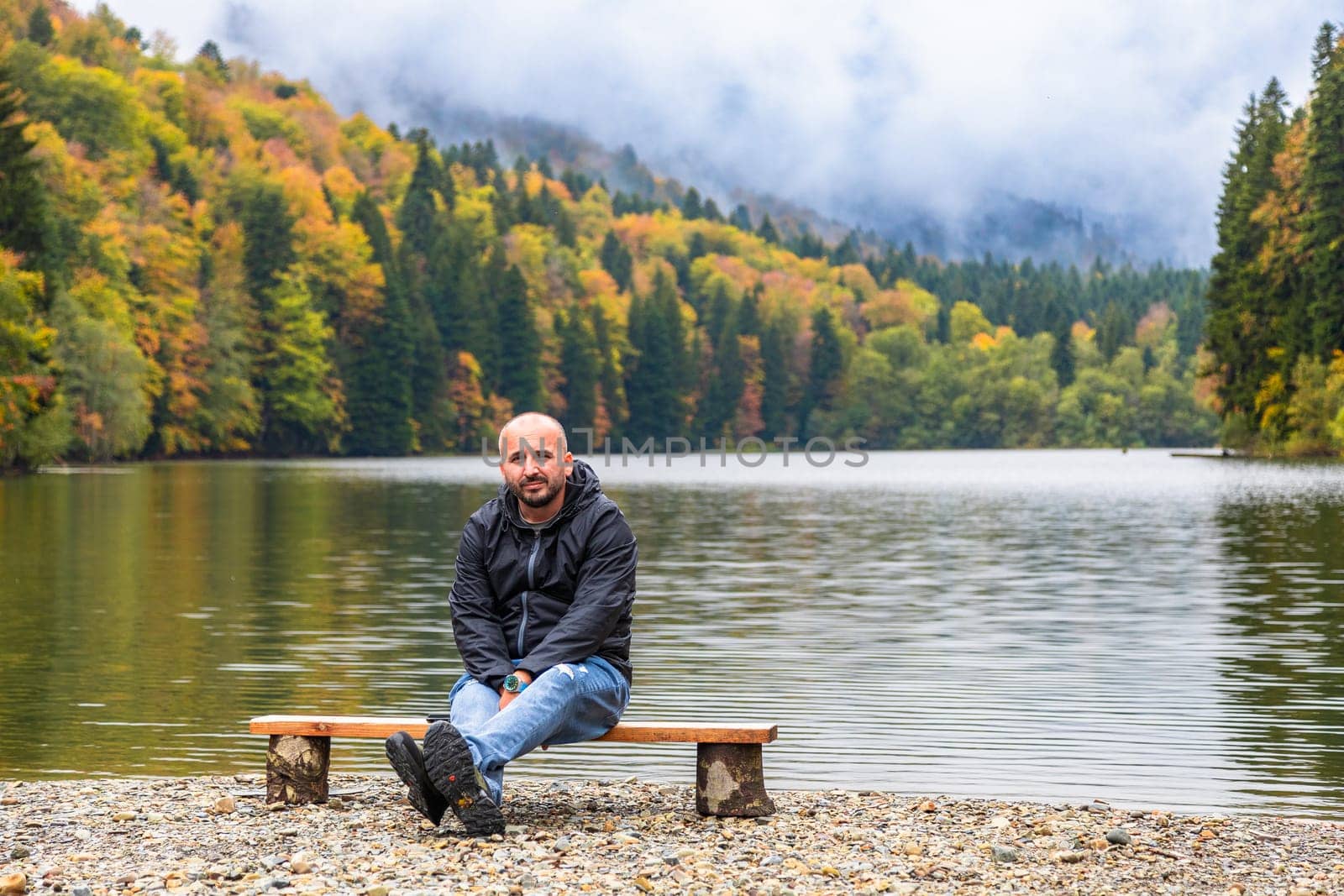 A man admires the picturesque scenery by the lake in the mountains, enjoying the tranquility and beauty of nature.