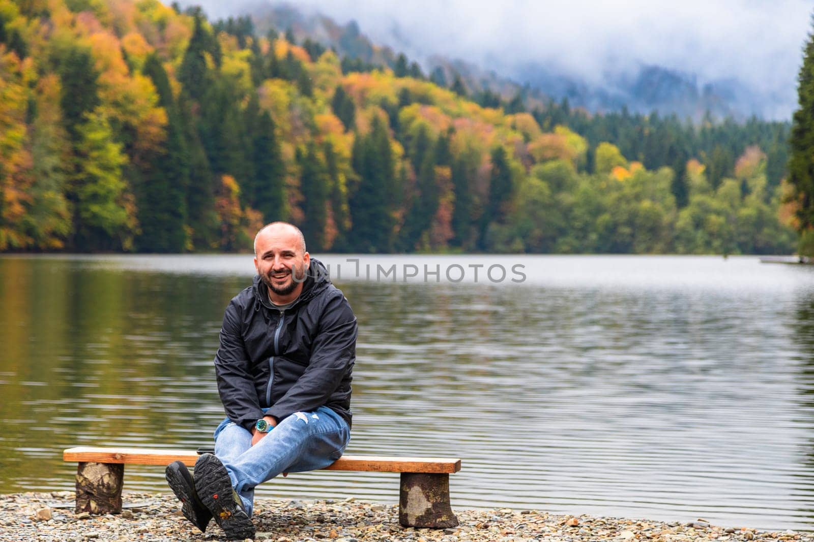 A man admires the picturesque scenery by the lake in the mountains, enjoying the tranquility and beauty of nature.