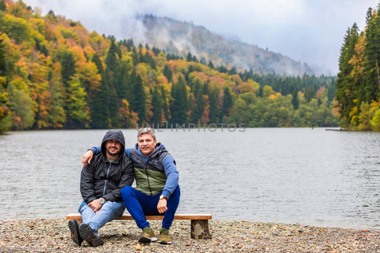 Two men enjoying the silence and the view of the autumn lake in the mountains.