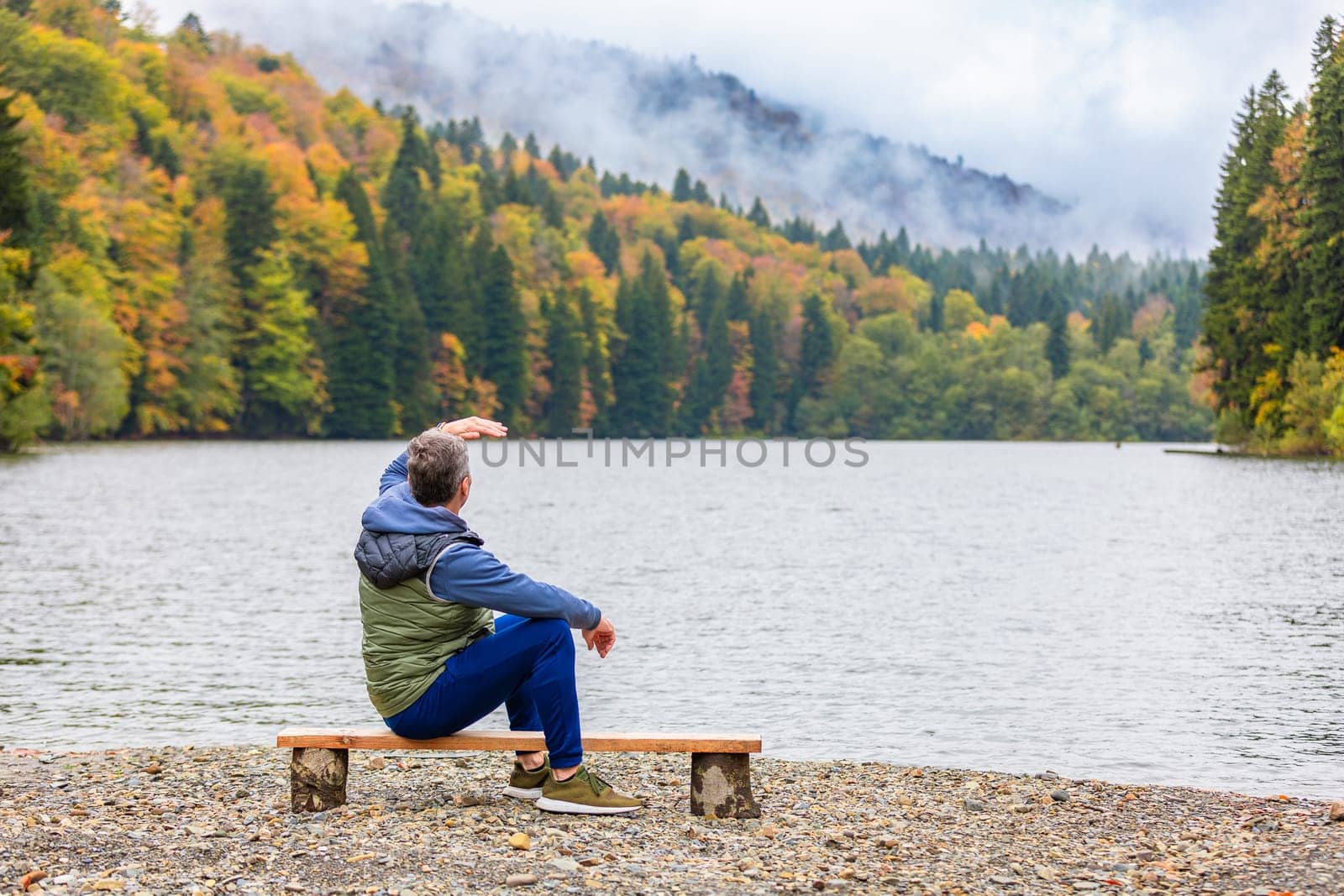 A man contemplates the beauty of nature by a lake in the mountains, plunging into the tranquility and beautiful views of the mountain landscape.