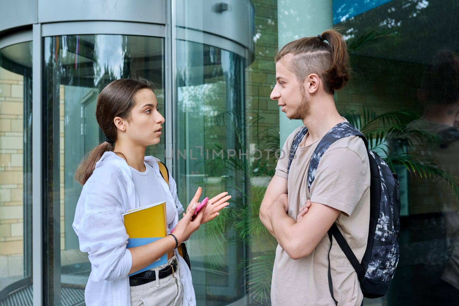 Meeting of two teenage students, guy and girl, near educational building by VH-studio