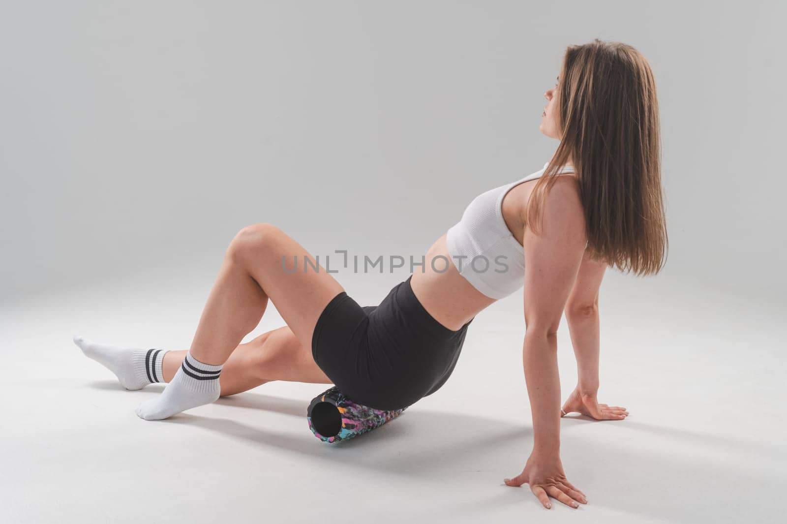 Caucasian woman doing roller exercise for myofascial release on white background. Self-massage of thighs