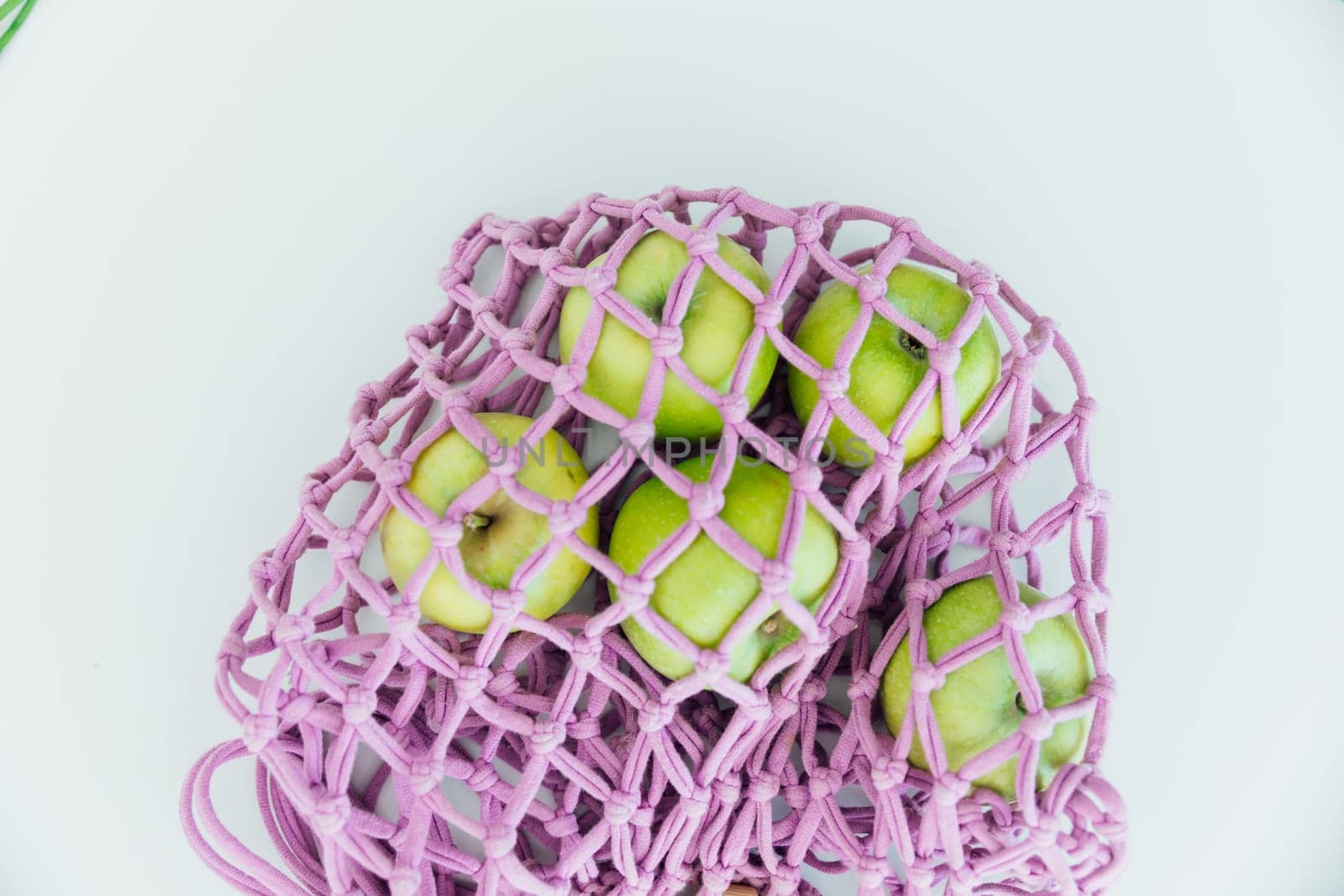 Five green apples in a mesh bag on a white background