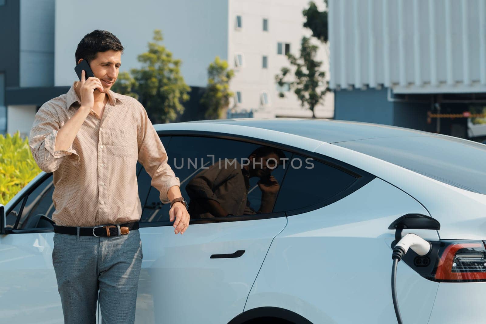 Young man recharge EV electric vehicle at green city park. Expedient by biancoblue