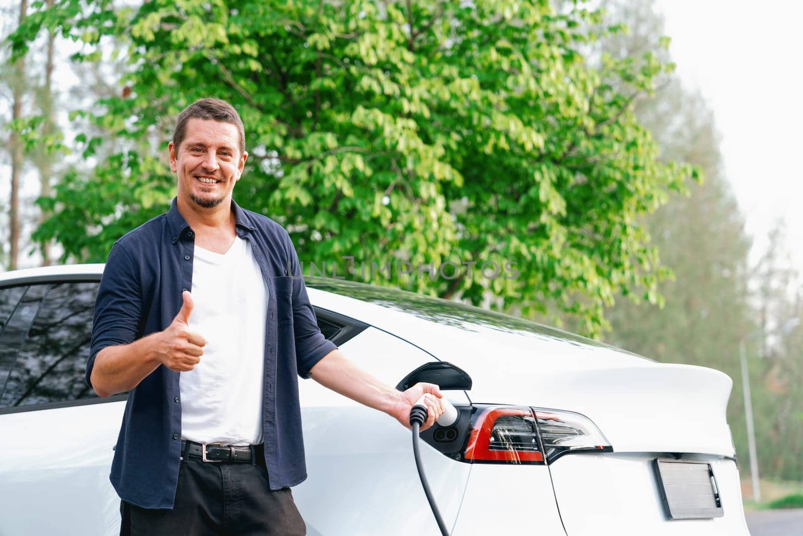 Man recharging battery for electric car during road trip. Exalt by biancoblue