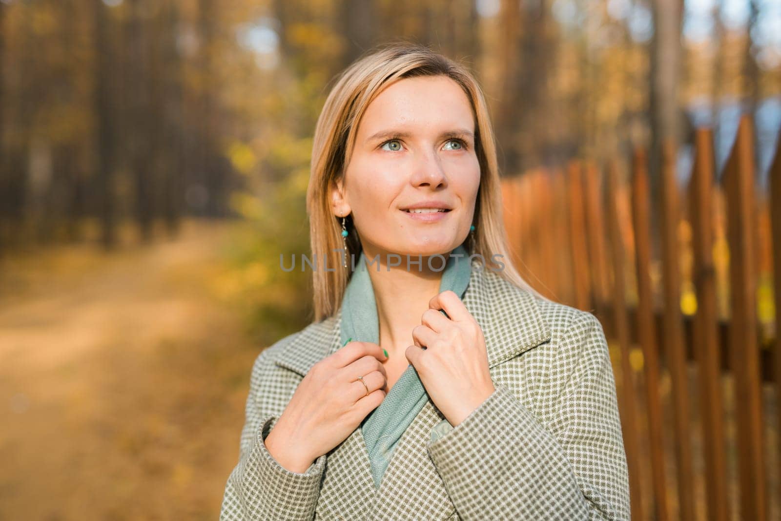 Blonde woman in elegant gray coat walks in the sunny autumn season park copy space mockup. Generation z and gen z youth concept. by Satura86