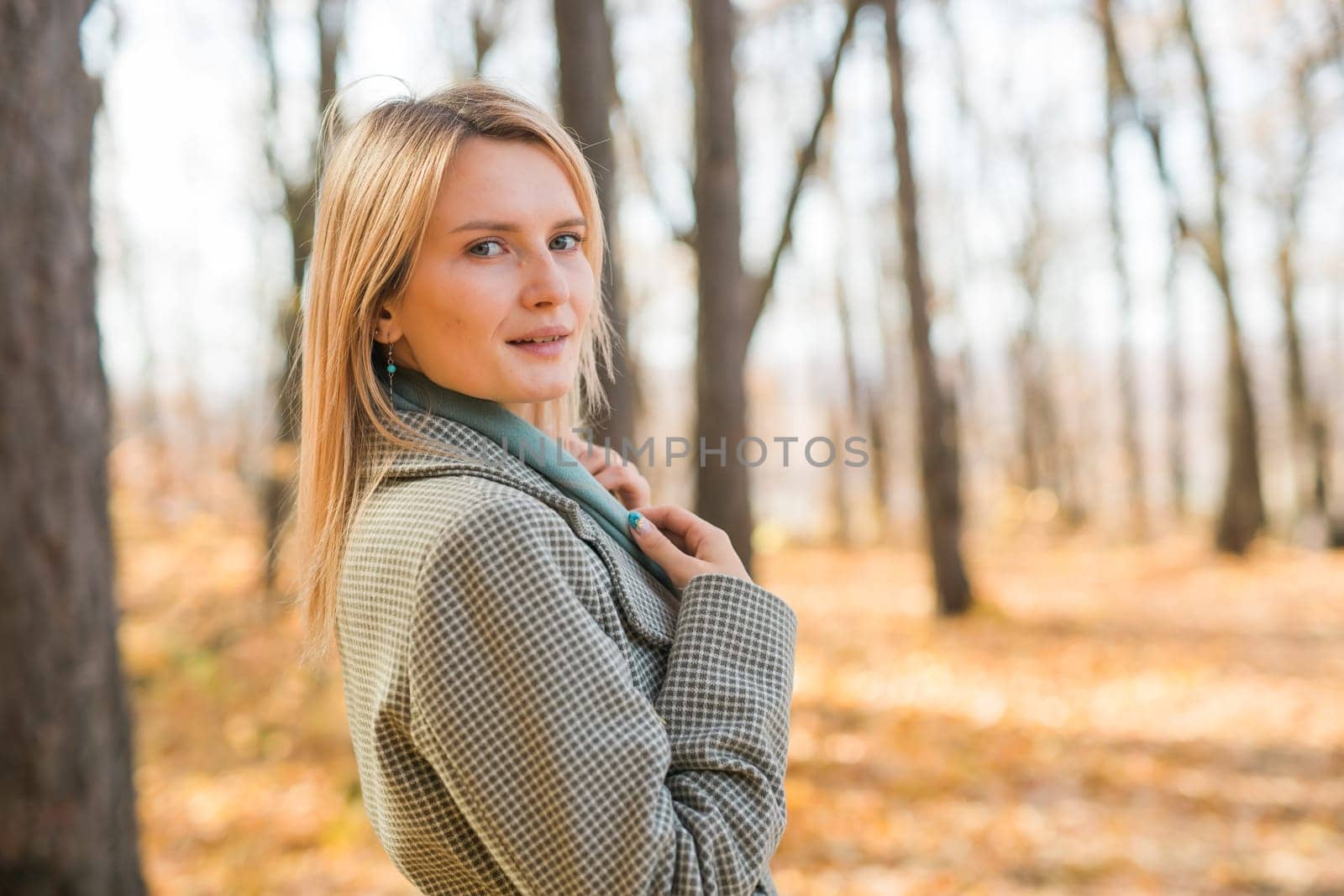 Blonde woman in elegant gray coat walks in the sunny autumn season park copy space mockup. Generation z and gen z youth concept. by Satura86