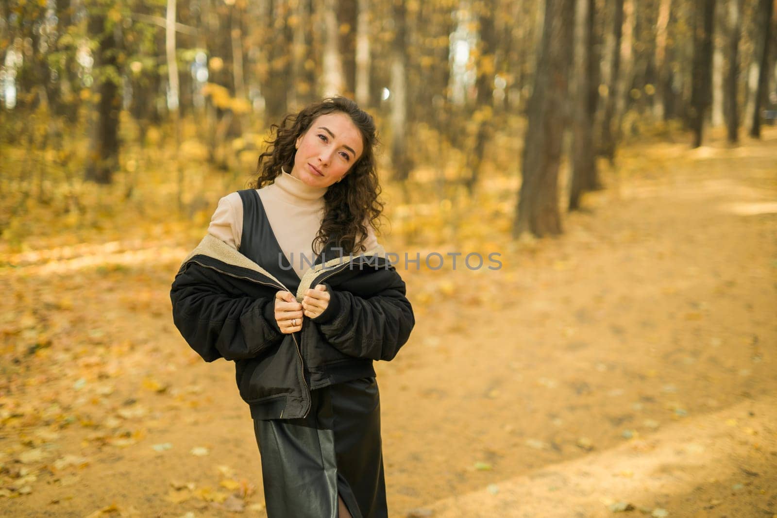 Attractive young woman walking in autumn park, happy mood and fashion style trend and curly long brown hair. Fall season and pretty female portrait copy space. Millennial generation concept by Satura86