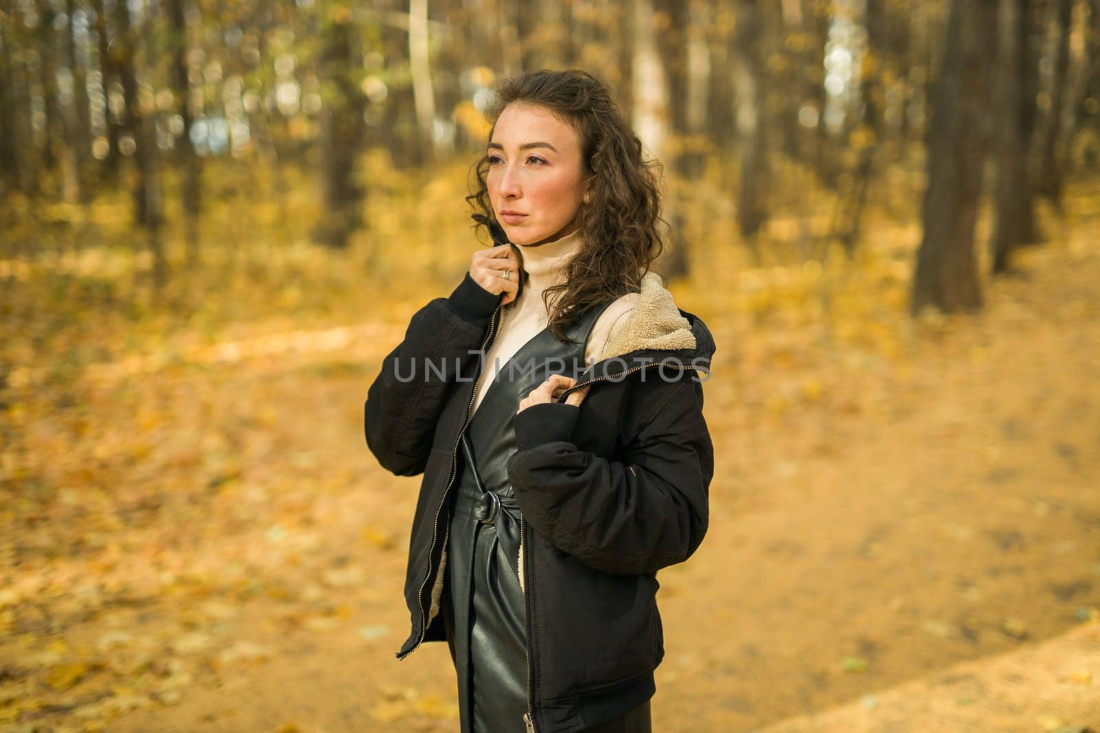 Attractive young woman walking in autumn park, happy mood and fashion style trend and curly long brown hair. Fall season and pretty female portrait. Millennial generation