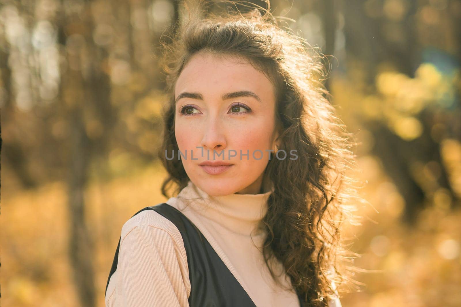 Attractive young woman walking in autumn park, happy mood and fashion style trend and curly long brown hair. Fall season and pretty female portrait copy space. Millennial generation concept by Satura86