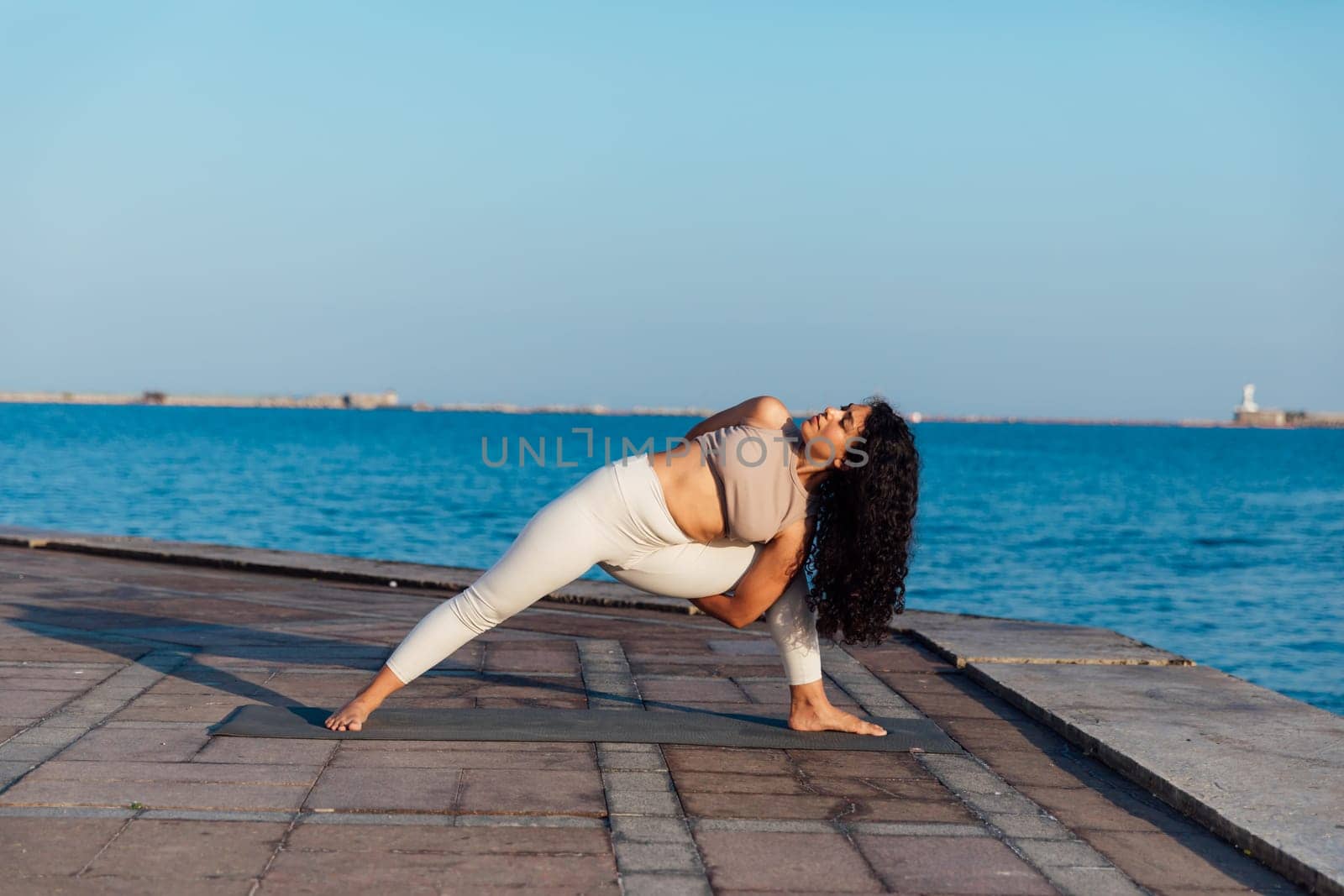 Woman doing yoga asana gymnastics breathing practice on the beach by the sea