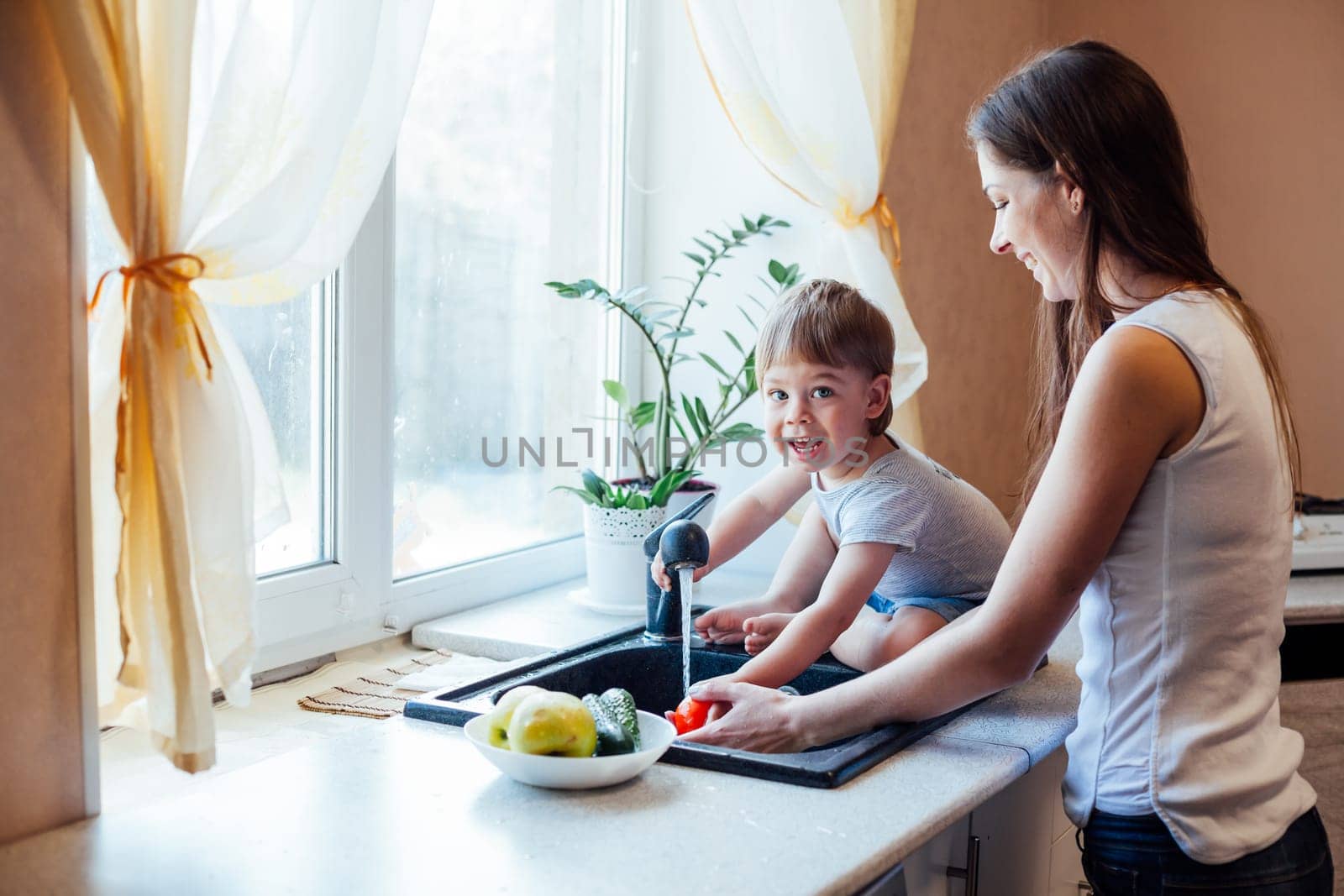 mother and young son wash their vegetables in the kitchen sink