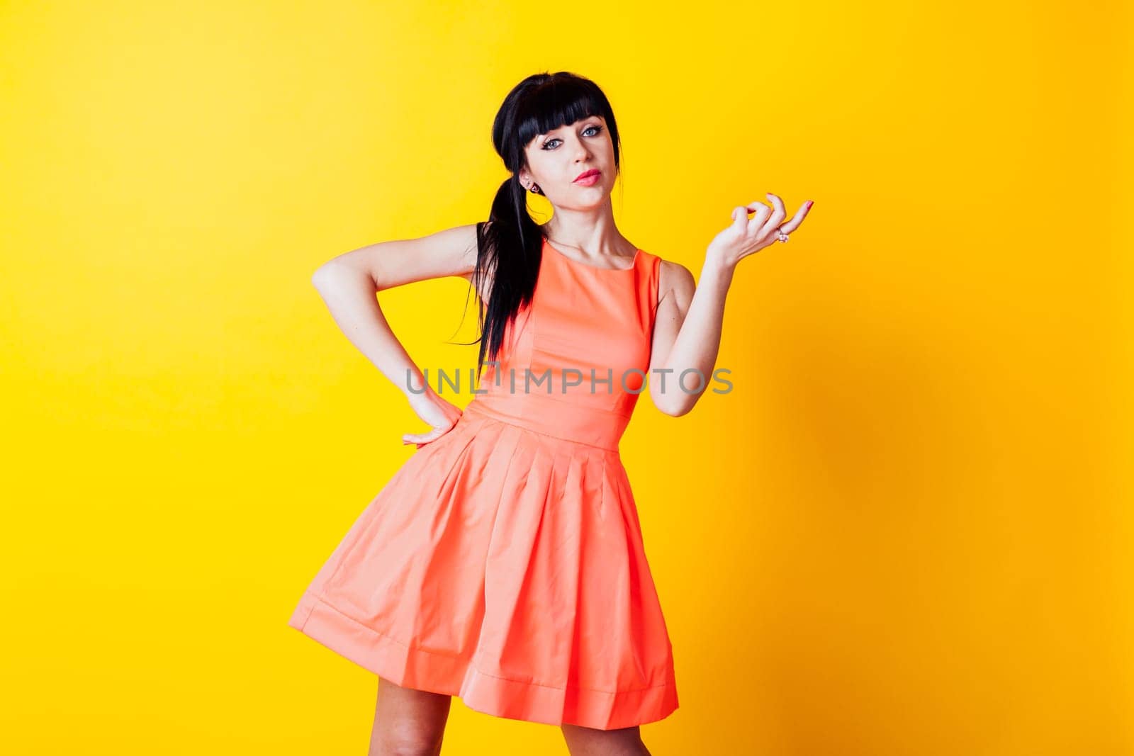 girl in orange dress on a yellow background hands up by Simakov