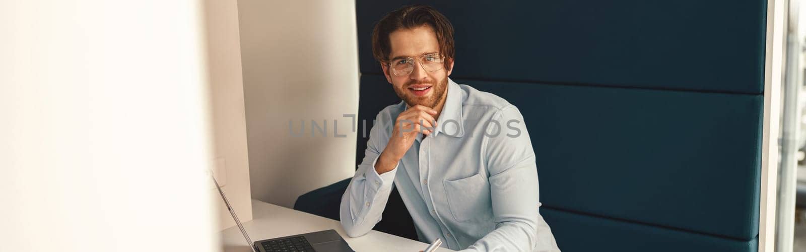 Smiling male manager drinking coffee during working on laptop in modern office . High quality photo