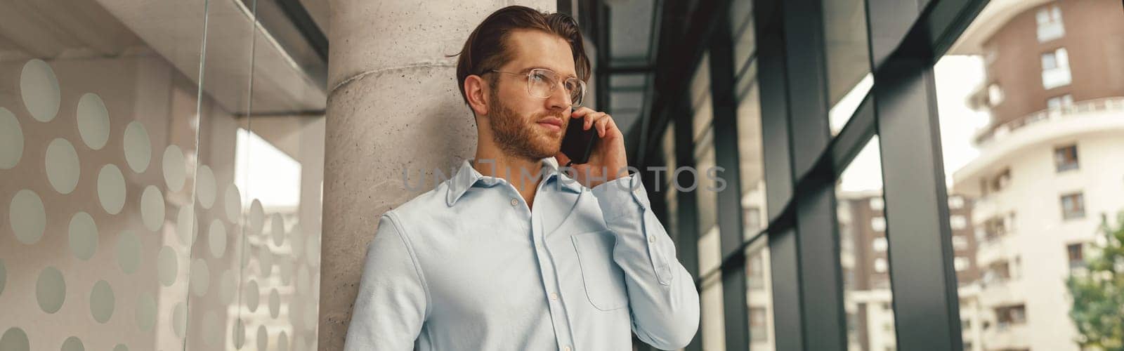 Male sales manager talking phone with client while standing in coworking and looking at side