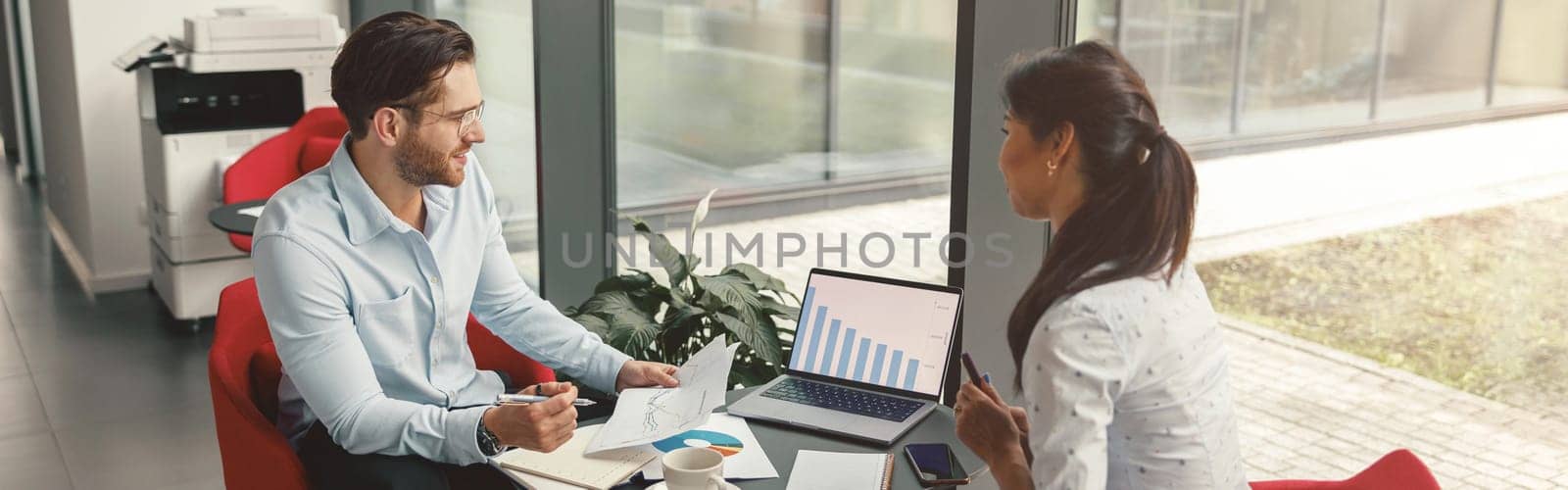 Two business colleagues working together with financial statements in stylish office near window