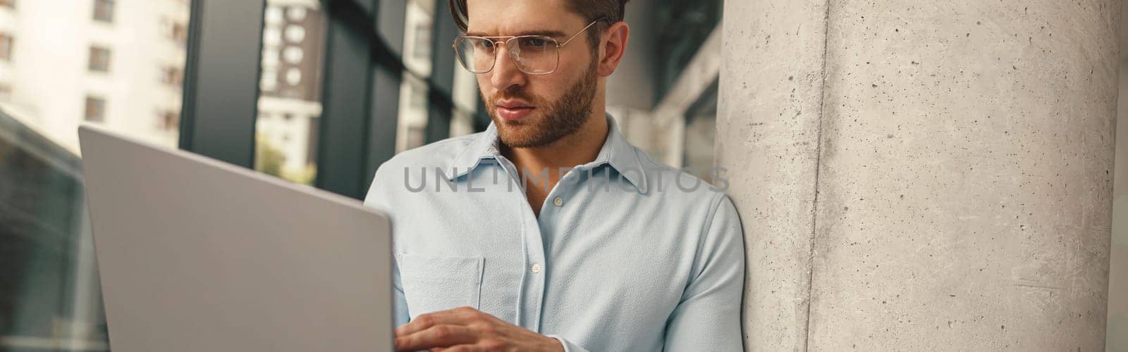 Handsome entrepreneur working on laptop standing in modern coworking during working day