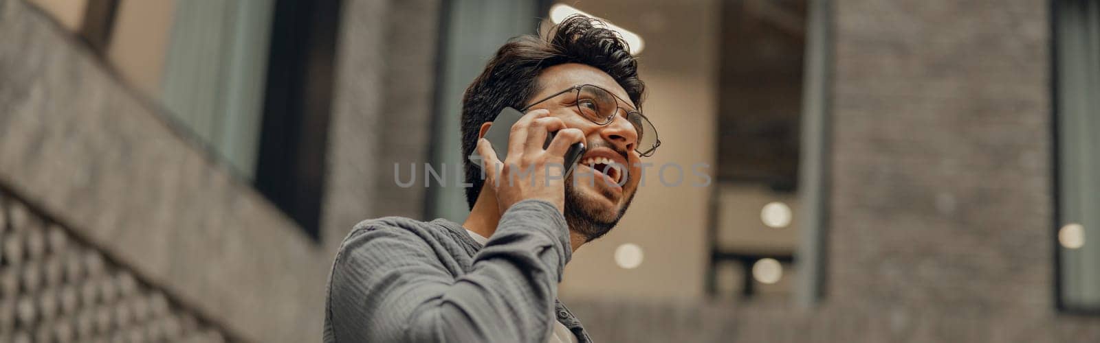 Bearded male freelancer in eyeglasses is talking phone standing in modern coworking space