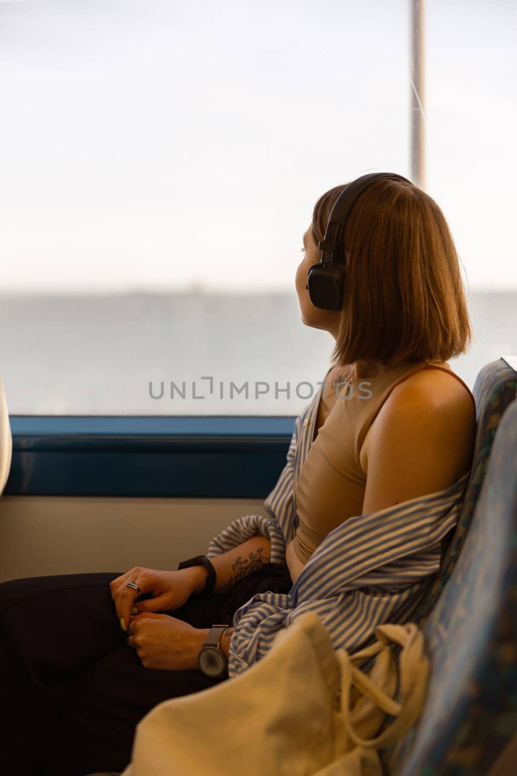 Woman in headphones while traveling in public transport and looking view outside the window by Yaroslav_astakhov
