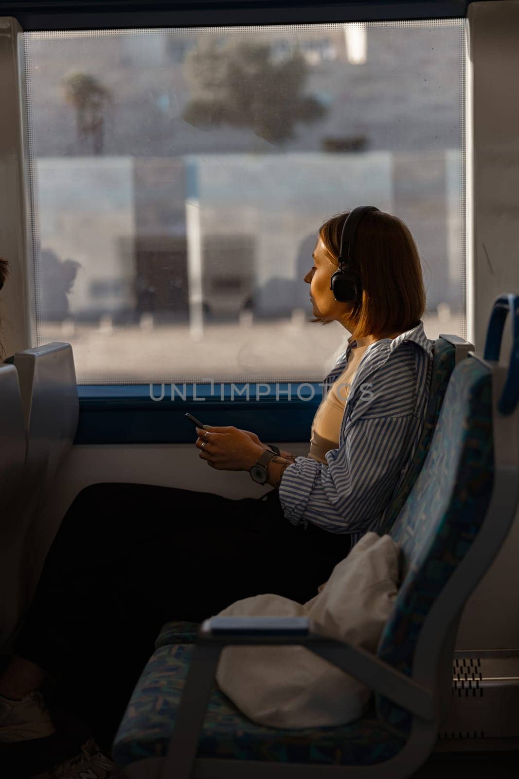 Woman in headphones while traveling in public transport and looking view outside the window by Yaroslav_astakhov