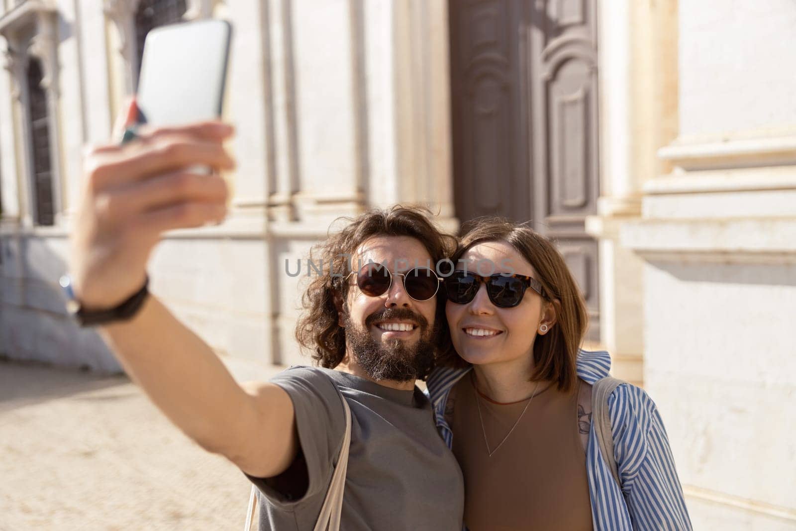 Happy tourist couple walking in city street and making selfie on phone. High quality photo
