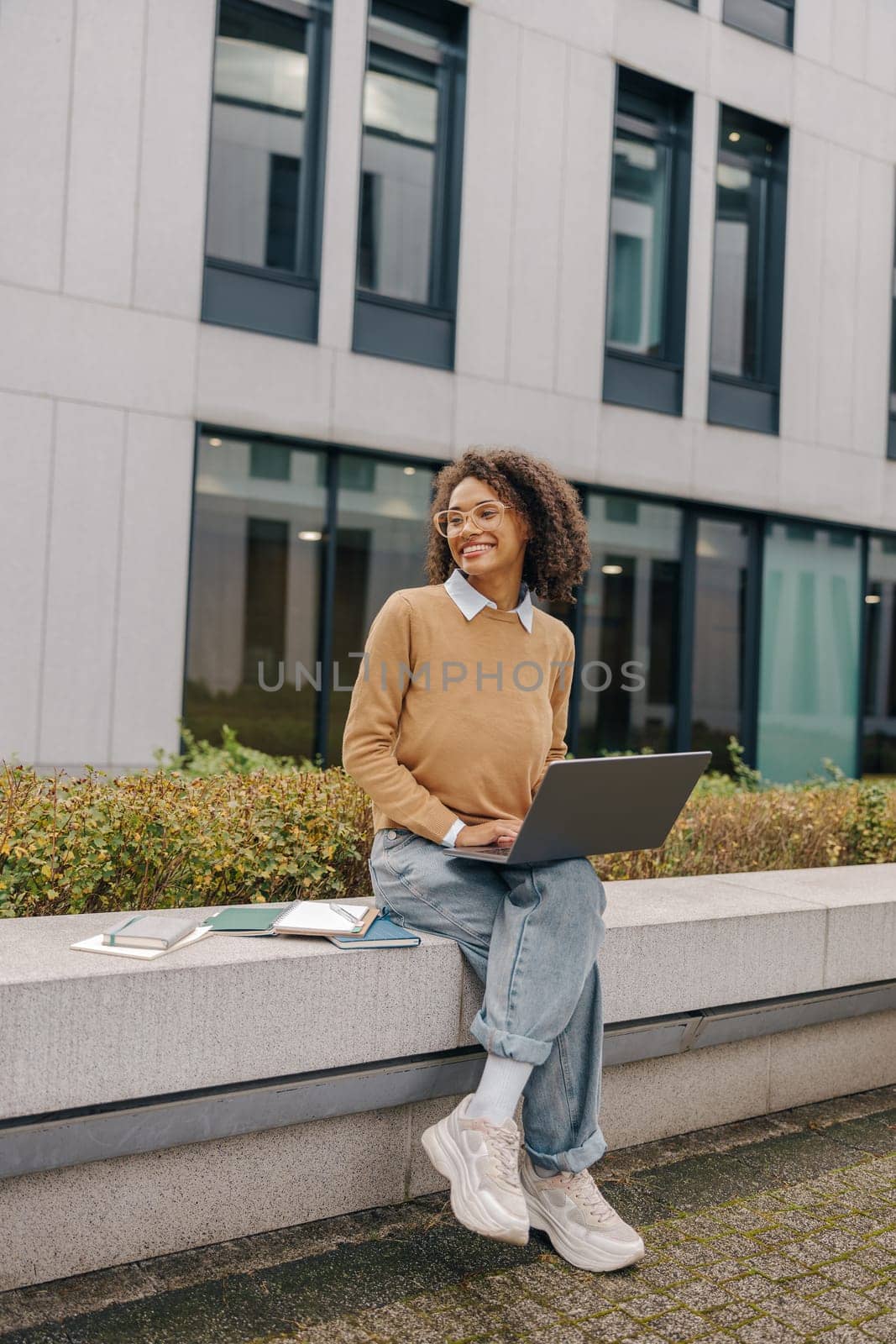 Smiling female freelancer working laptop while sitting outside on background of office building