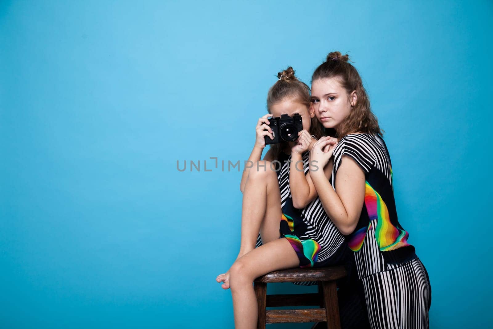 Two fashionable girls with a camera on a blue background