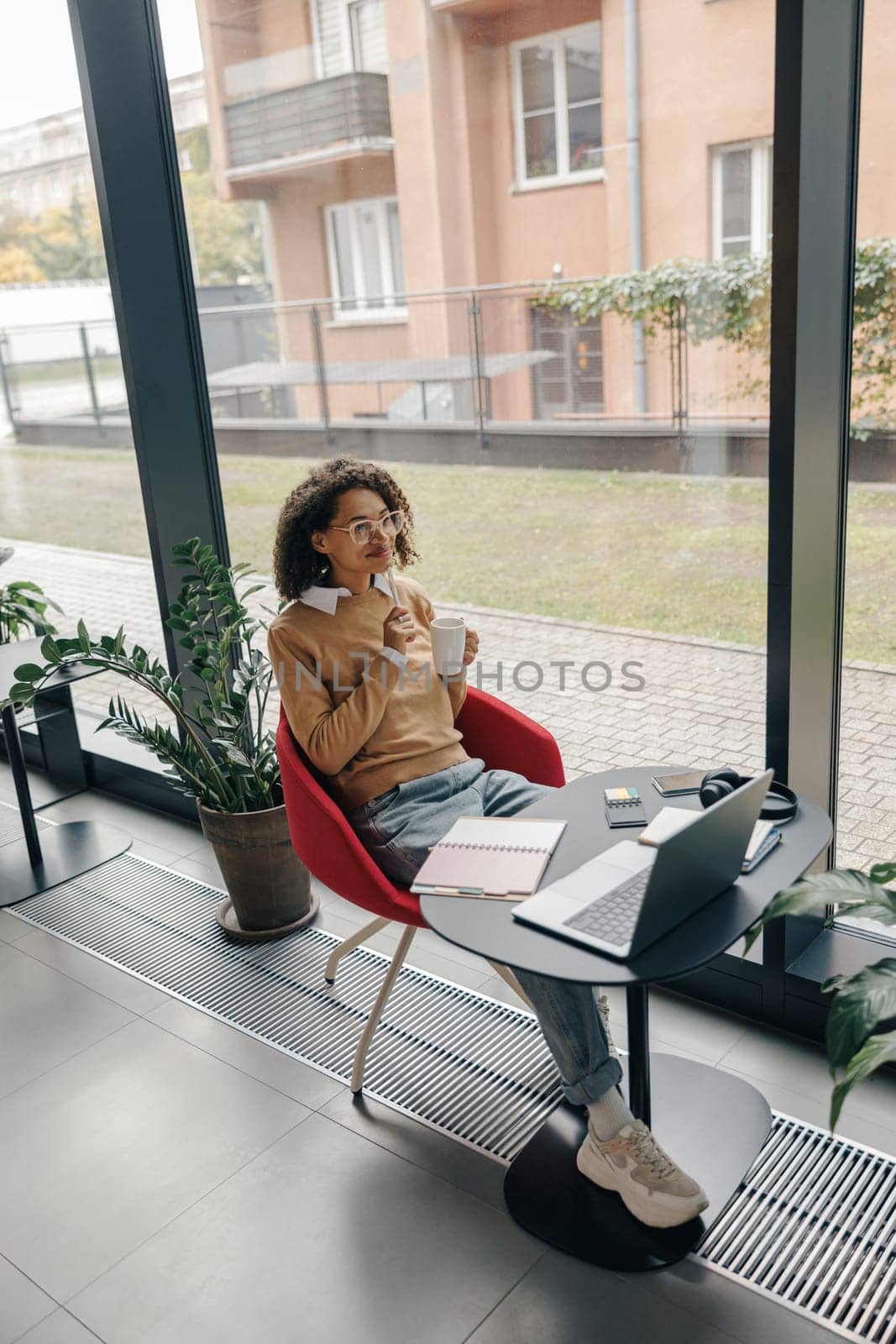 Smiling woman entrepreneur working on laptop, making notes in cozy coworking space interior