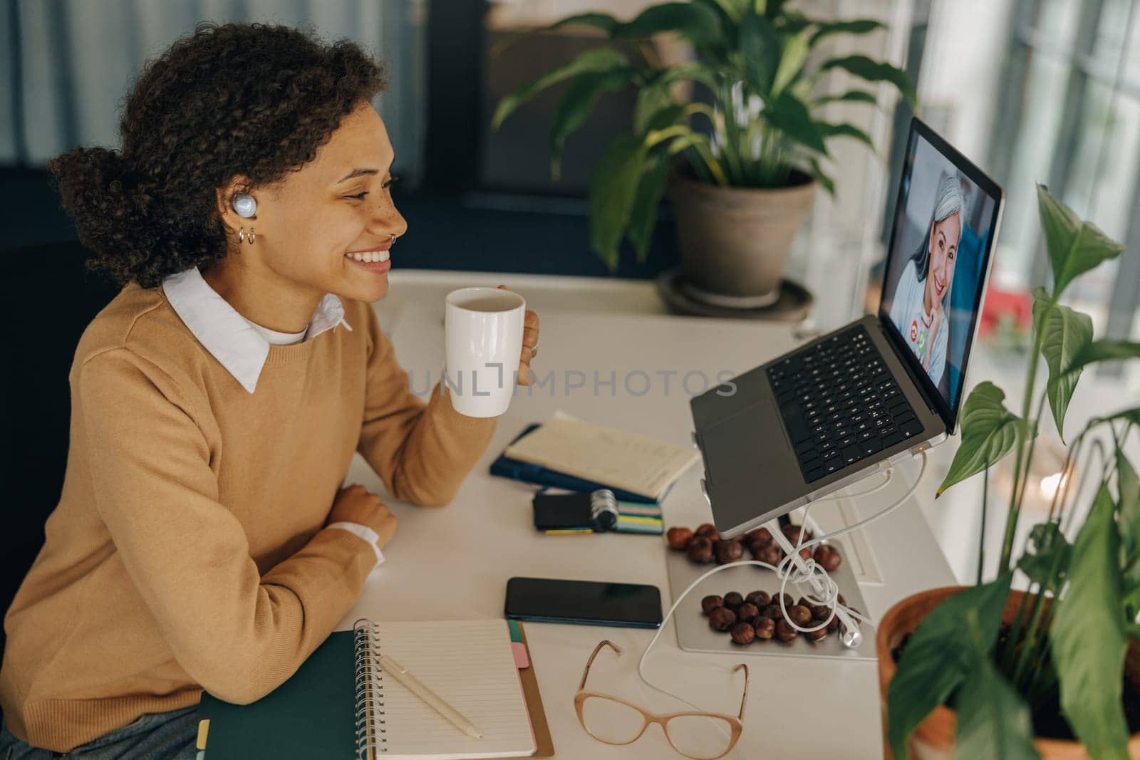 Smiling female freelancer have video conference with client and drinking coffee sitting in coworking by Yaroslav_astakhov
